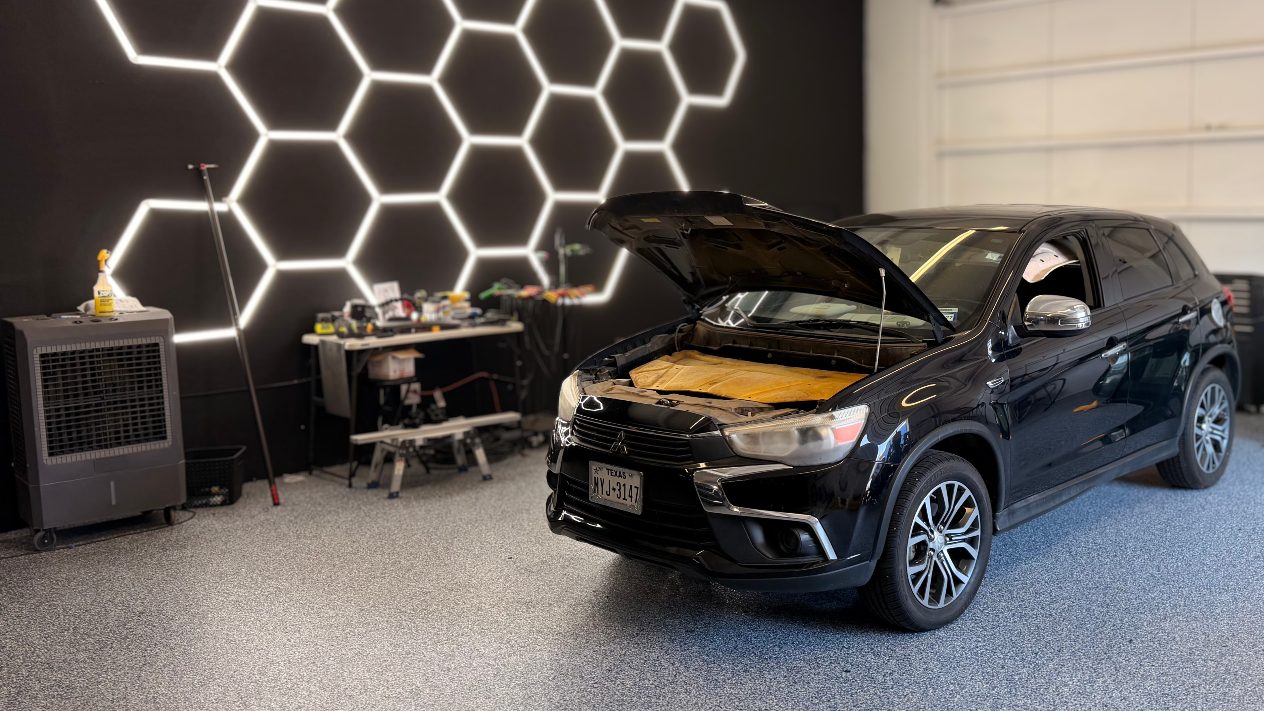 A black crossover with its hood open in the shop bay, under the hexagon LED ceiling