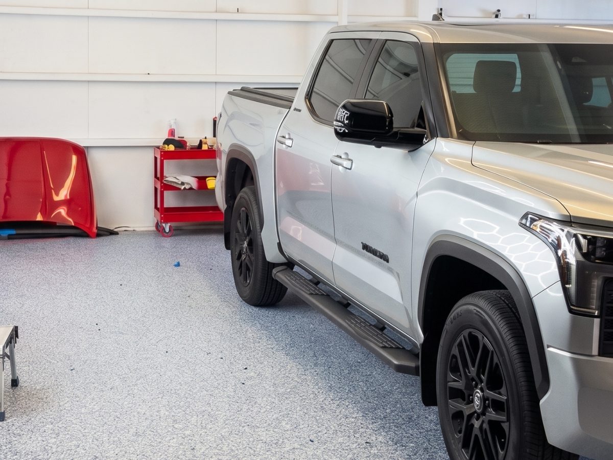 A silver pickup in the bay beside a removed red body panel propped against the wall